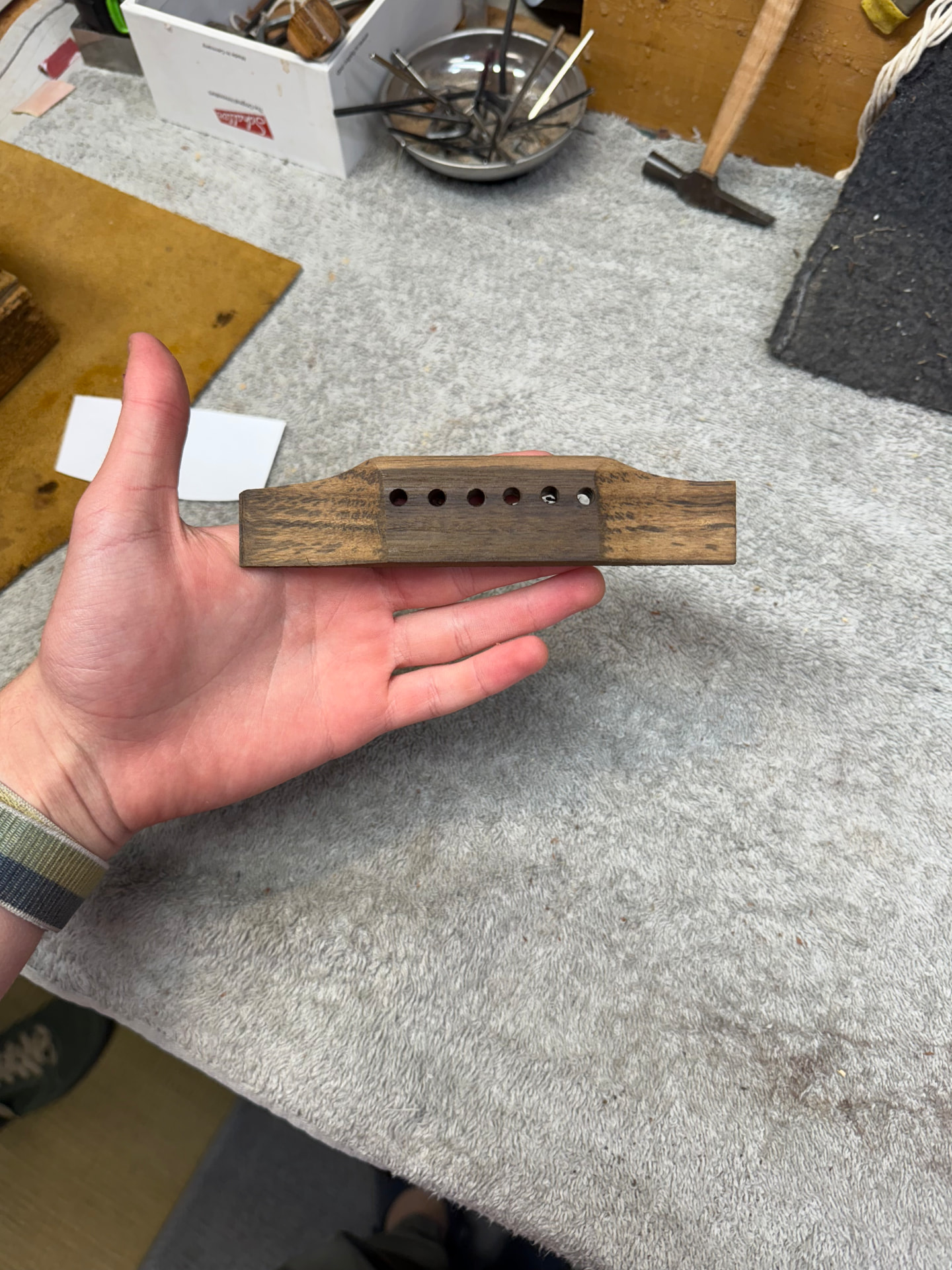 Hand holding the carved wooden bridge with string holes drilled