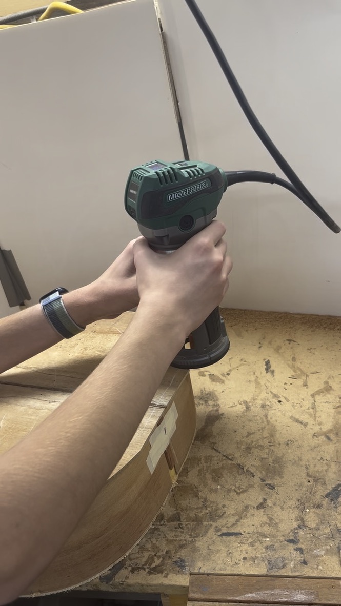 Trimming the excess wood from the guitar body edge with a handheld router