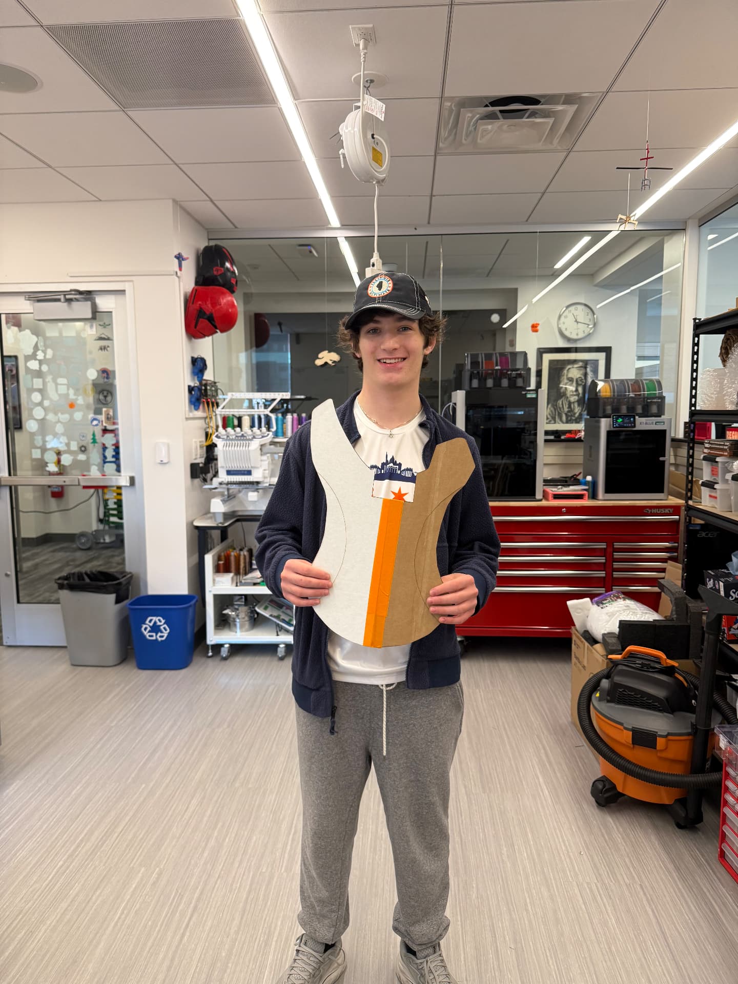 Holding the cardboard scale model of the guitar in the makerspace