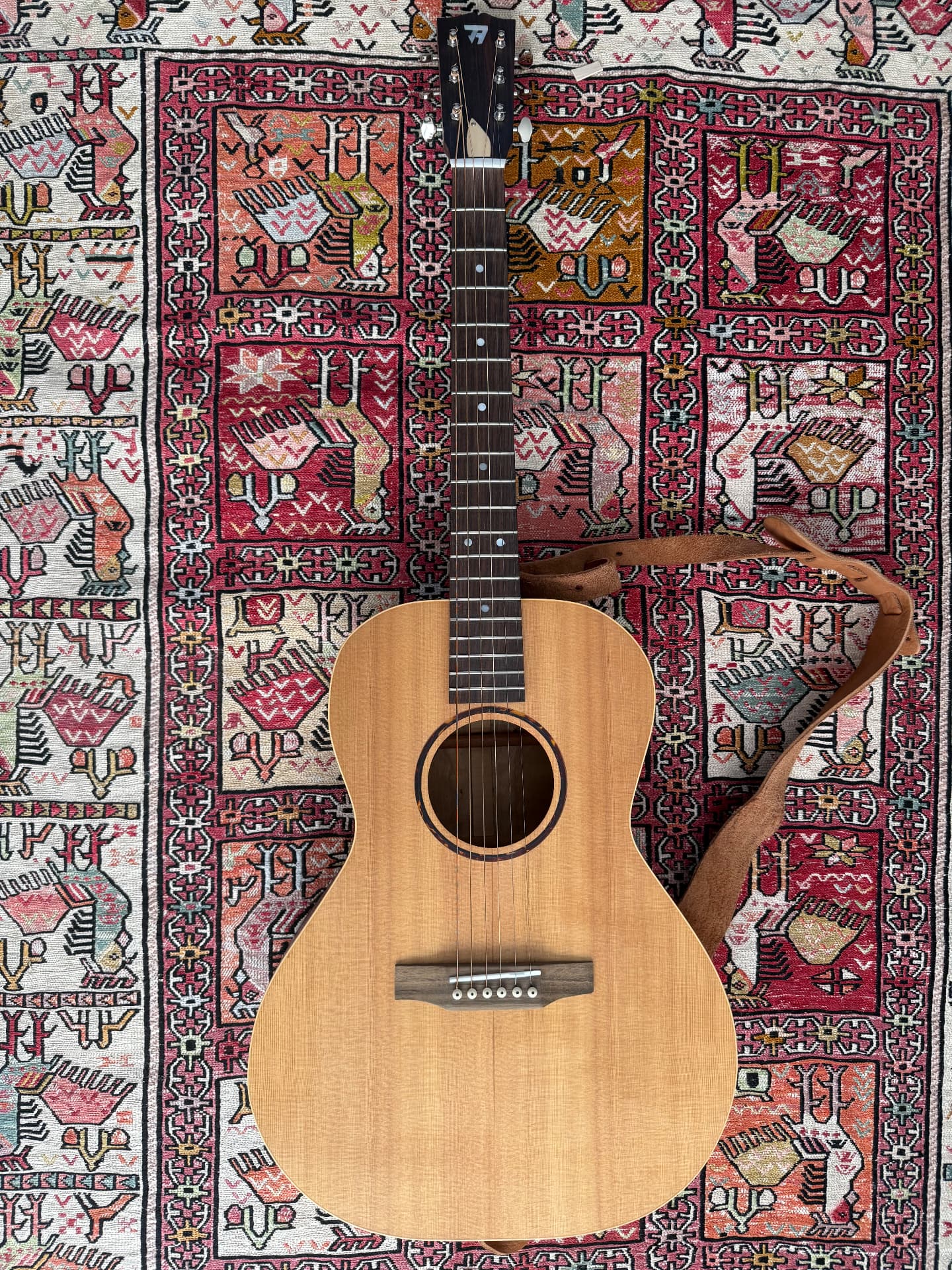 Custom-built acoustic guitar laid on a patterned rug