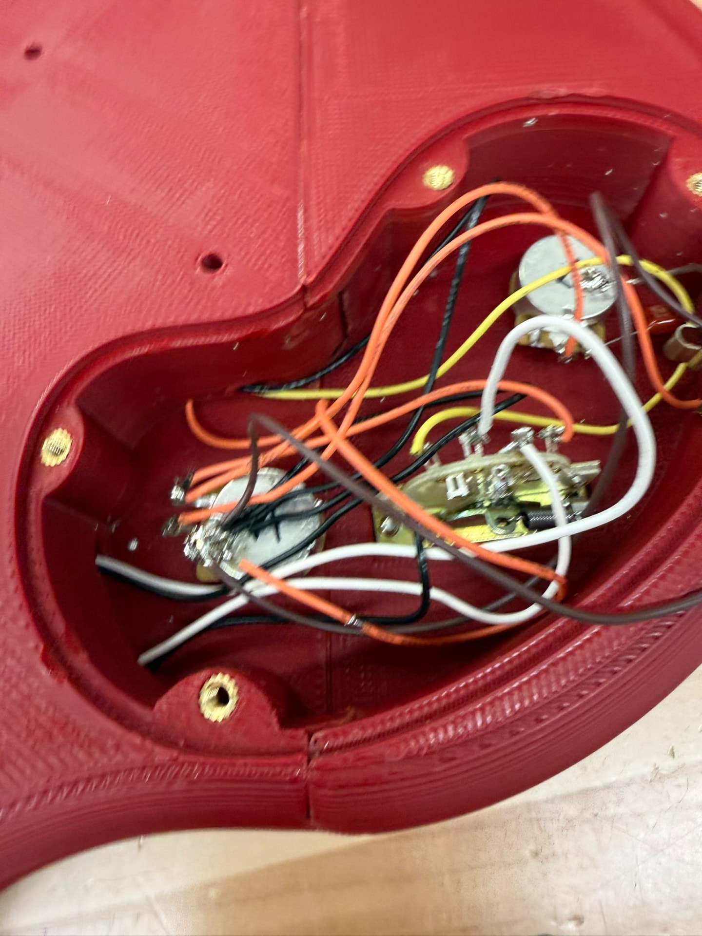Close-up into the rear electronics cavity of the 3D-printed guitar body, showing potentiometers, a pickup selector switch, soldered wires, and brass threaded inserts along the rim
