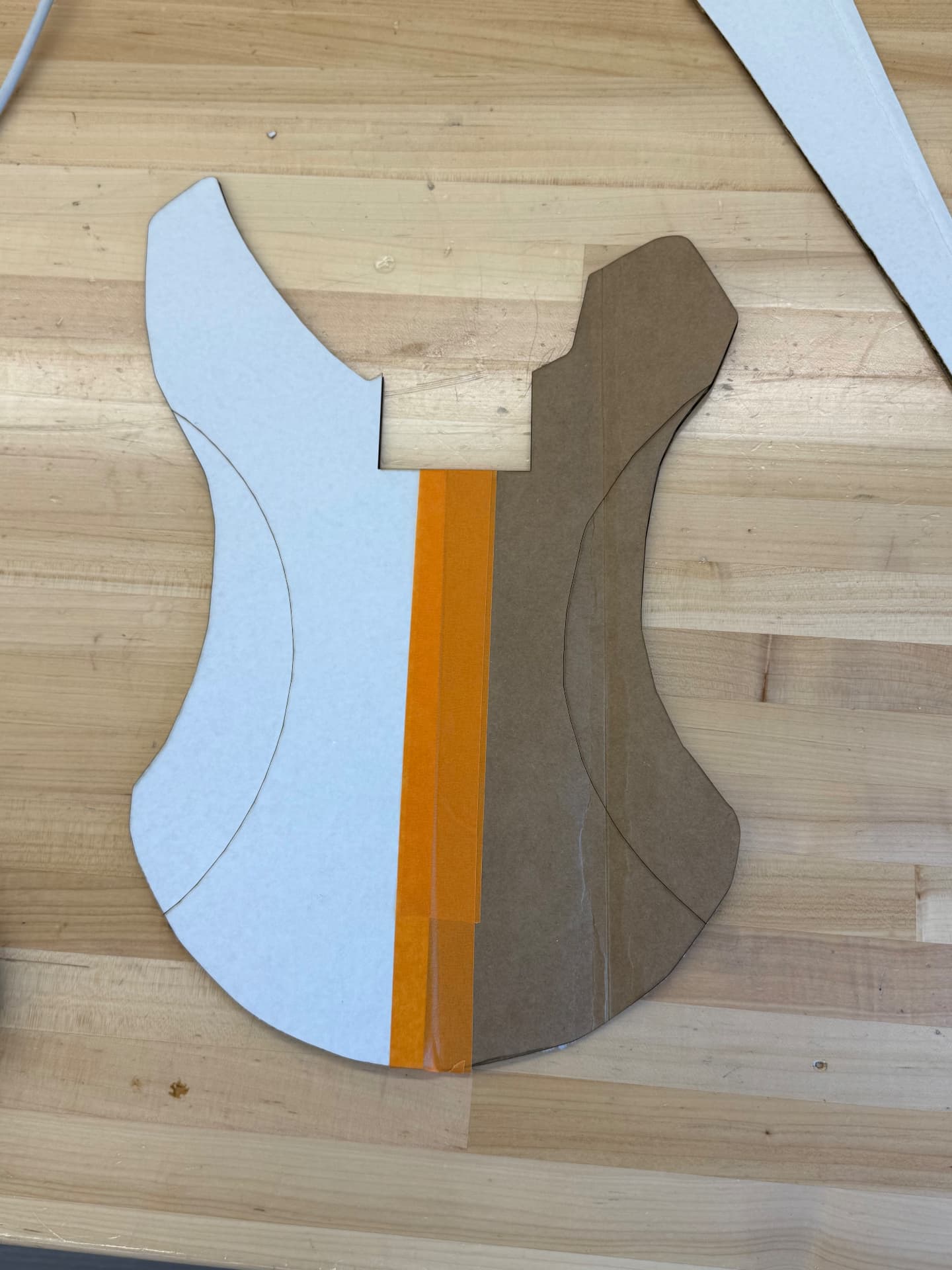 Cardboard and paper cutouts of the guitar body taped together on a wooden workbench