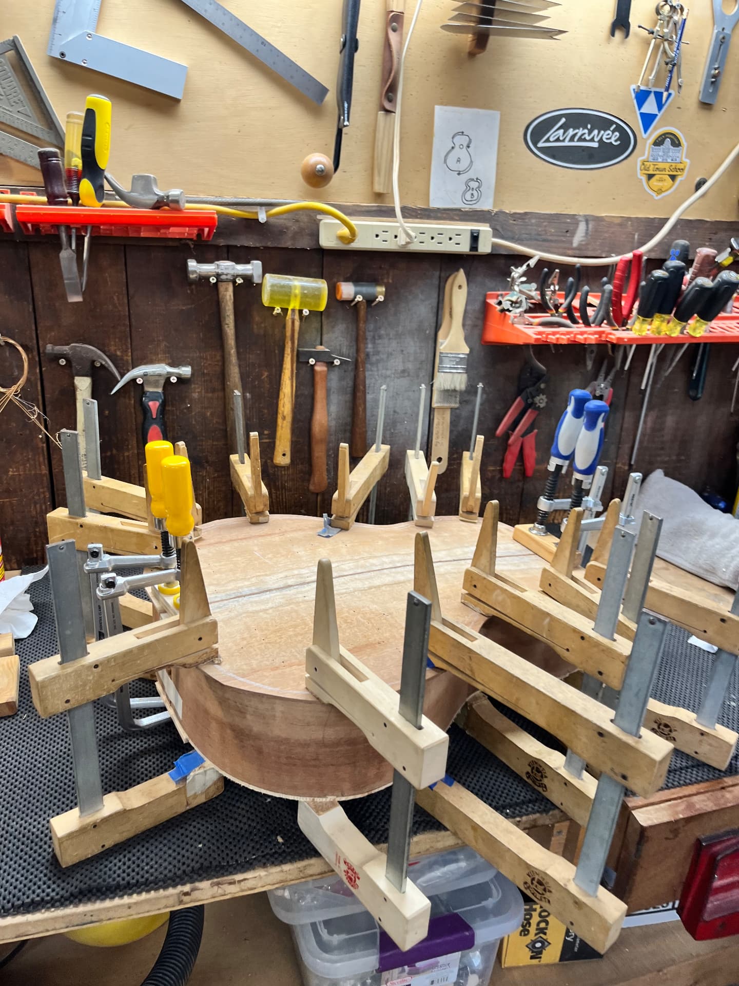 Guitar body glued and clamped in the workshop with tools on the wall behind
